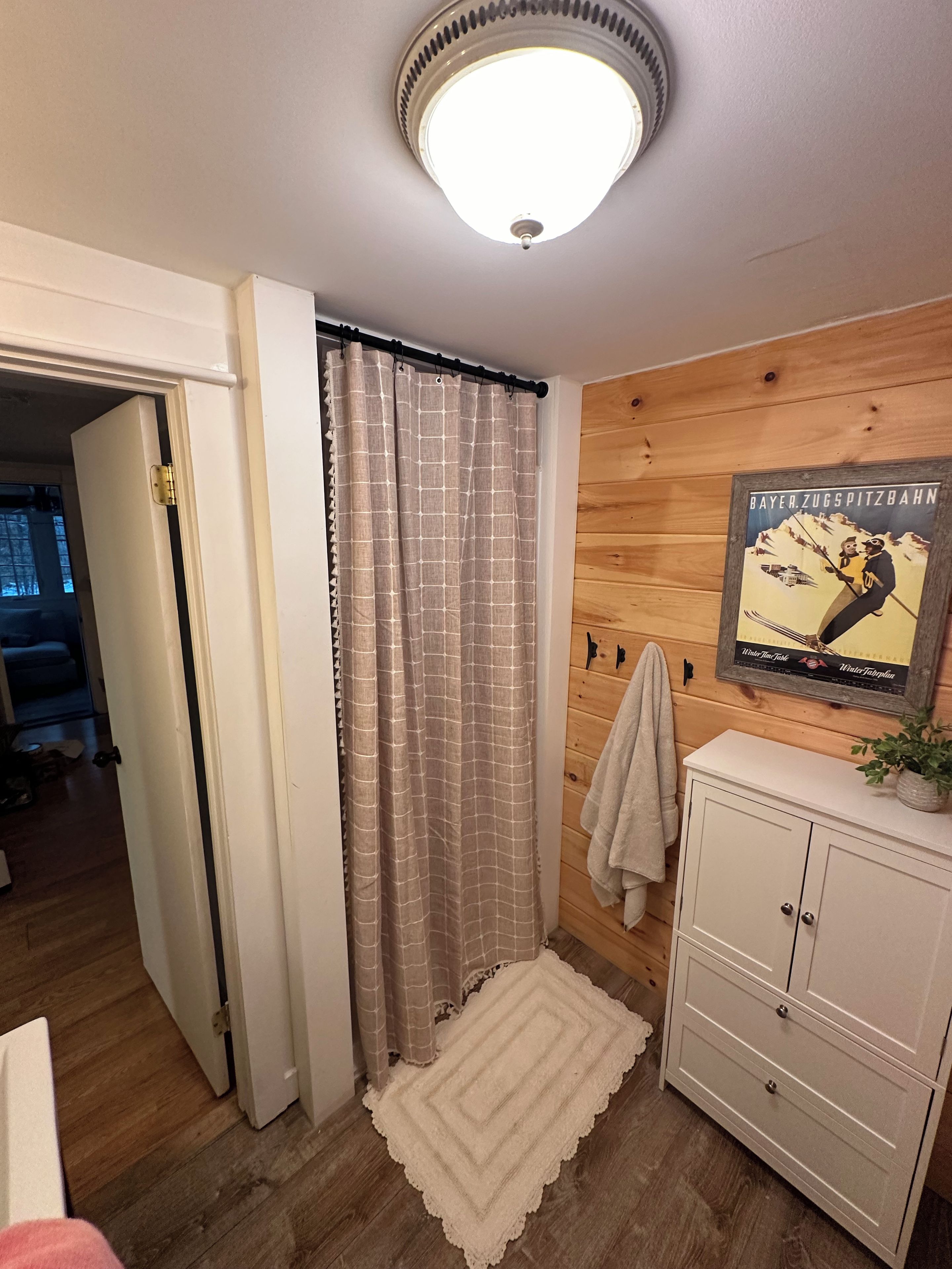 A bathroom with a wooden wall, a shower curtain, a white cabinet, and a poster on the wall.