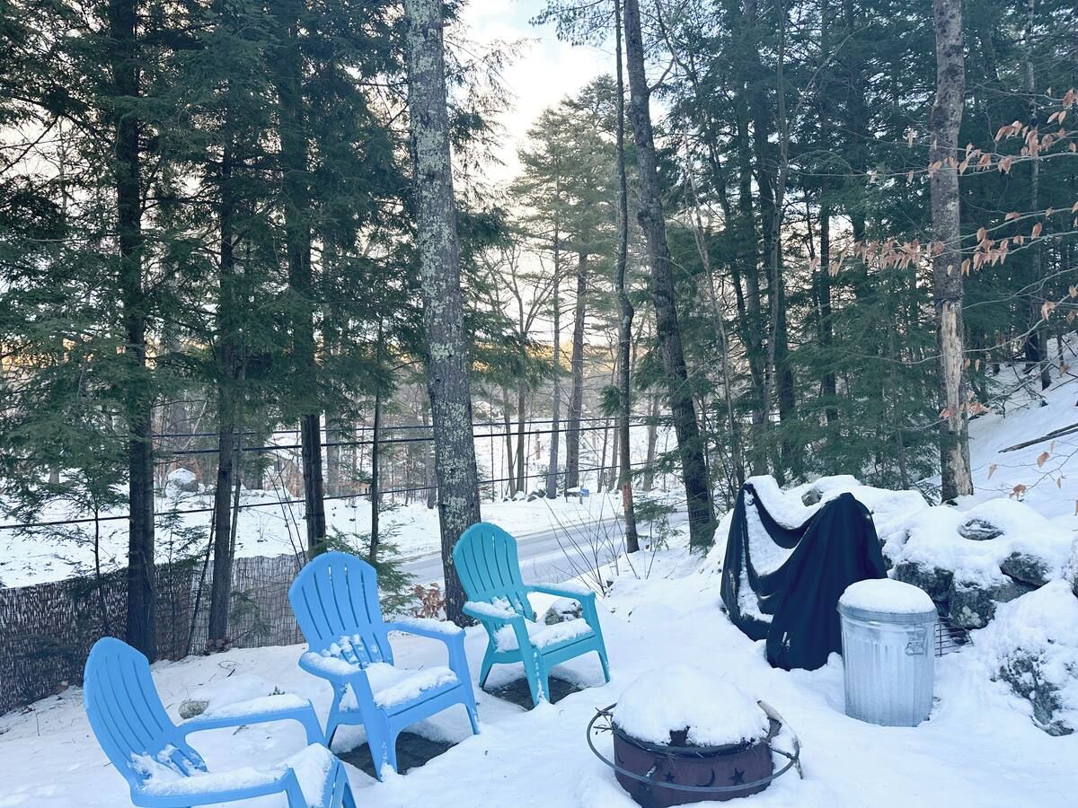 Un área de estar al aire libre cubierta de nieve, con sillas Adirondack y un cubo de basura metálico.