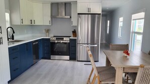 A modern kitchen with white and blue cabinets, stainless steel appliances, and a dining area with wicker chairs. - Cozy Keys Hideaway on the water (Tavernier)