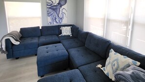 A modern living room with a sectional sofa, a ceiling fan, and a large window. - Cozy Keys Hideaway on the water (Tavernier)