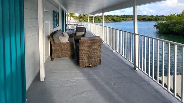 A covered outdoor area with a table and chairs, a railing, and a view of a body of water. - Cozy Keys Hideaway on the water (Tavernier)