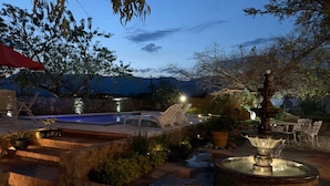 A pool area with a fountain, lounge chairs, and a stone wall.
