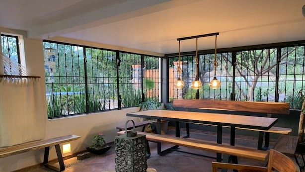 A spacious patio with a wooden bench, a round wooden table, and hanging pendant lights.