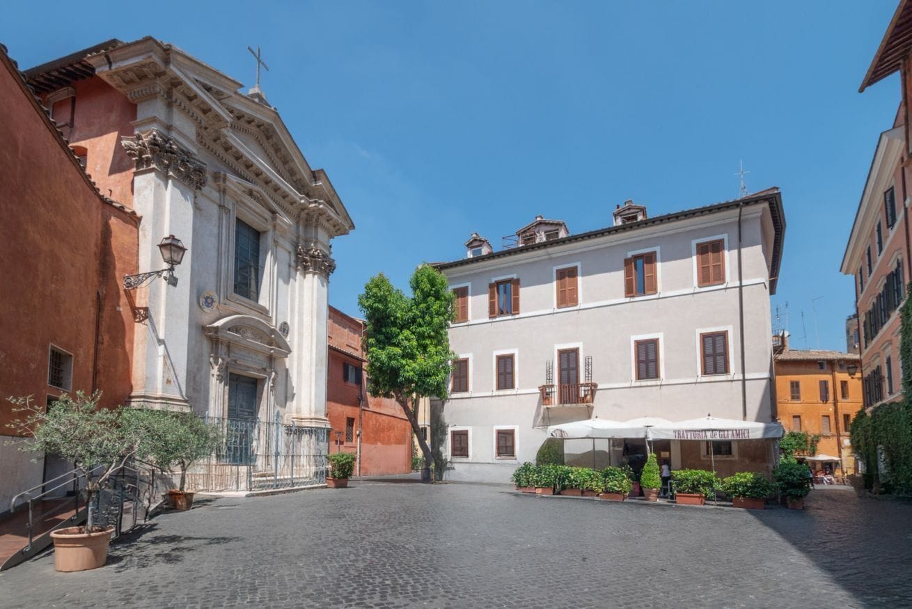 A cobblestone street with historic buildings, a church with classical architecture, and a cafe with outdoor seating.