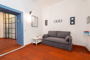 A living room with a grey sofa, a small white side table, a framed quote on the wall, and a blue door.