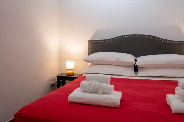 A neatly made bed with white linens, a red bedspread, and a bedside lamp. - Number Five Apartment in Trastevere (Roma)