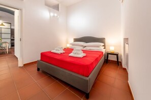 A hotel room with a bed, a nightstand, a lamp, and a view of the dining area. - Number Five Apartment in Trastevere (Roma)