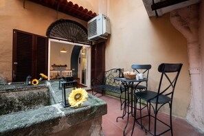 An outdoor seating area with a stone bench, a table with chairs, and an air conditioning unit mounted on the wall. - Number Five Apartment in Trastevere (Roma)
