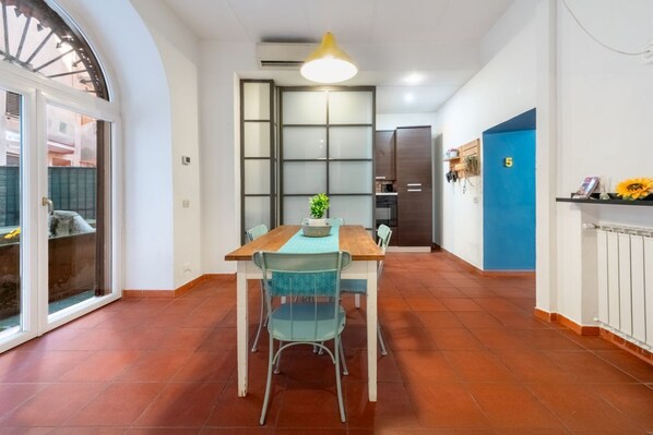 A dining area with a table and chairs, a ceiling light, a blue door, and a window with a view.