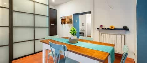 Un comedor con una mesa de madera y sillas azules, una planta en maceta y una estantería con objetos.