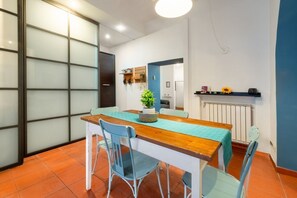 A dining area with a wooden table and blue chairs, a potted plant, and a shelf with items. - Number Five Apartment in Trastevere (Roma)
