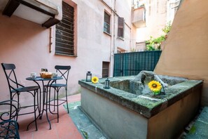 A small outdoor seating area with a table and chairs, a stone bench, and a flower vase.