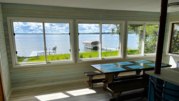 A room with a large window overlooking a lake, a wooden table with blue placemats, and a bench.