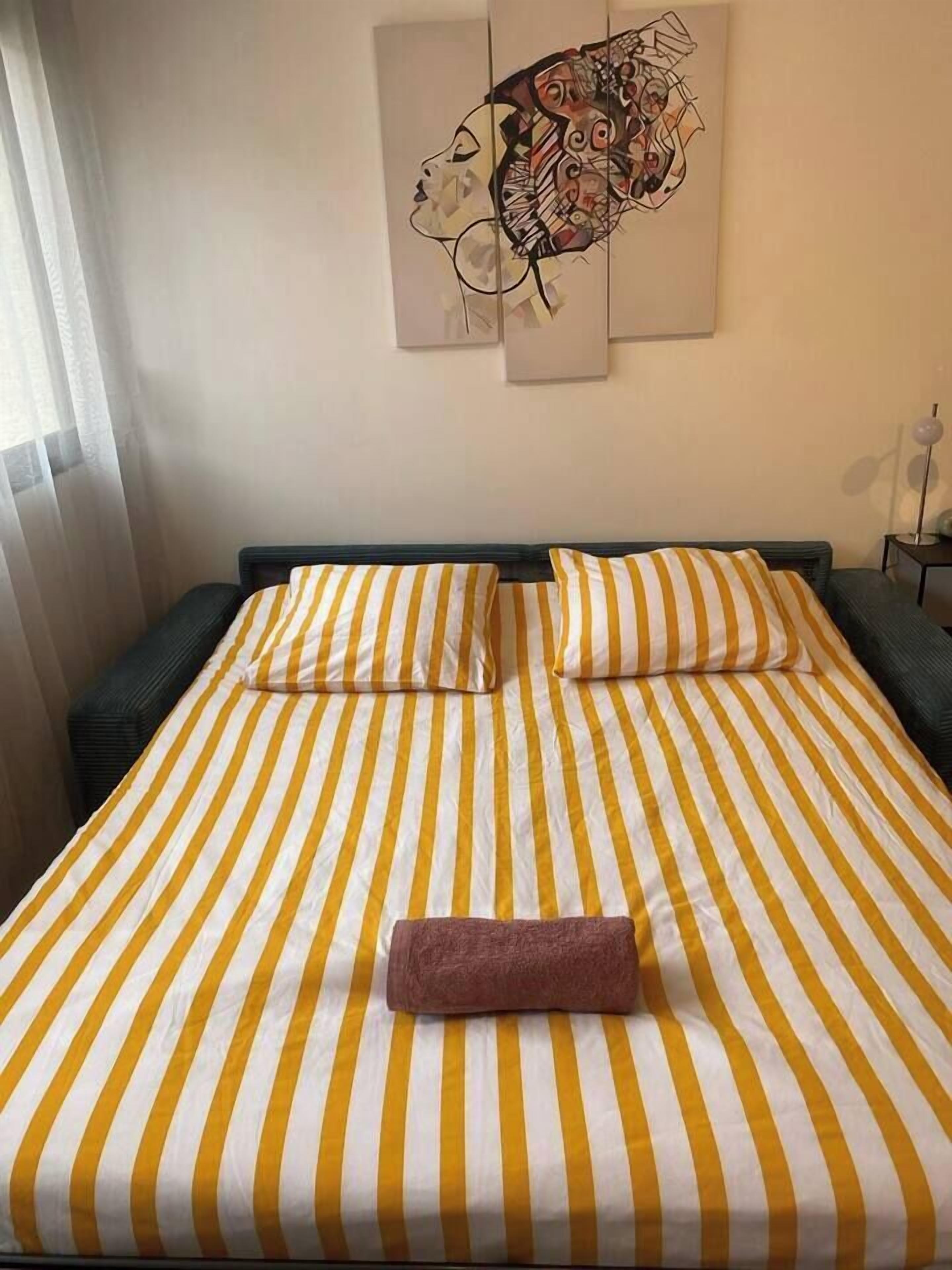 A bed with yellow and white striped bedding, a brown towel, and a wall art piece above it.