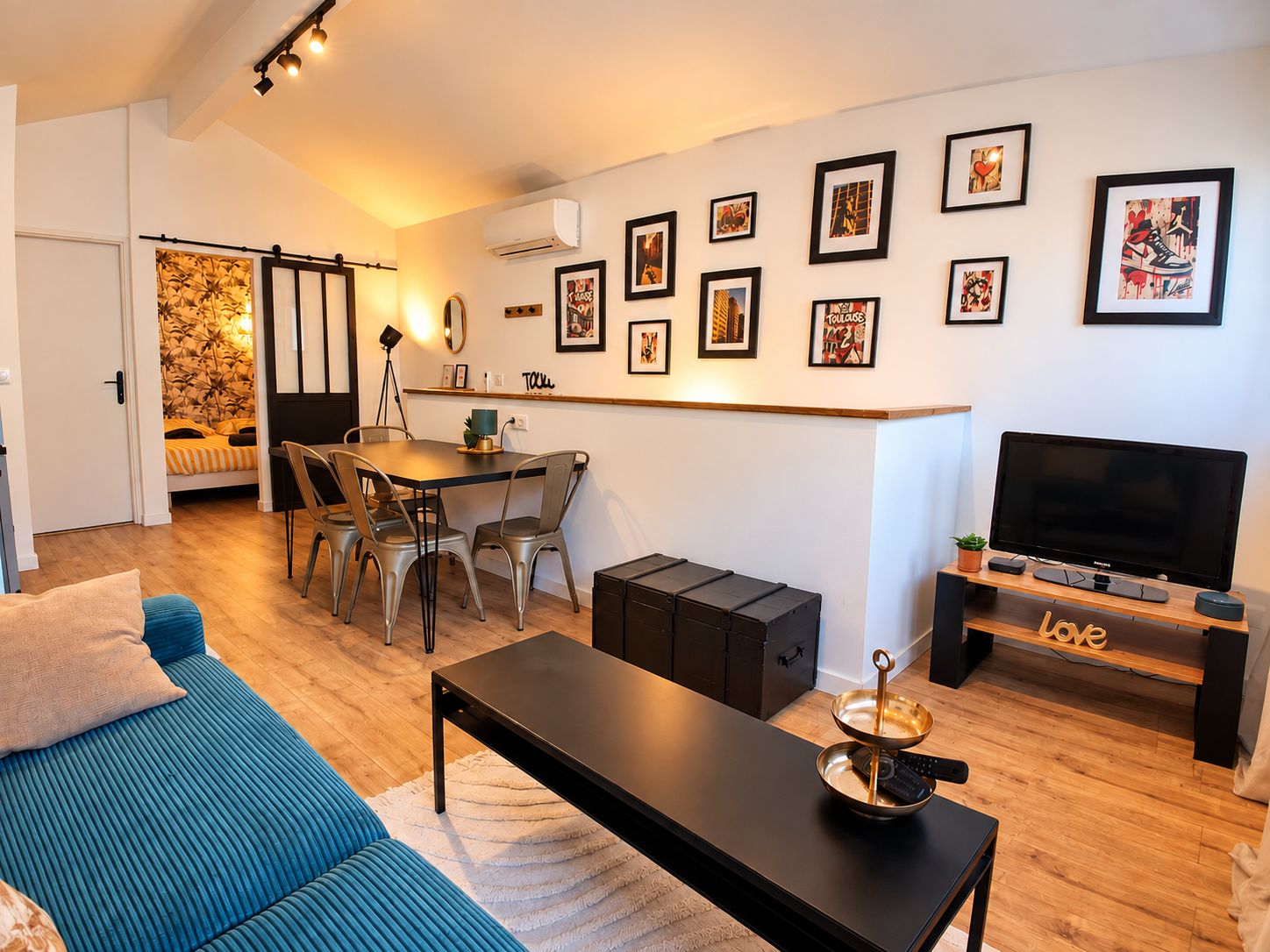 A modern living space with a sofa, a dining table with chairs, a TV, and a wall adorned with framed pictures.
