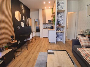 A modern living room with a sofa, a coffee table, and a TV. There is a kitchen area with a microwave and a refrigerator. - At Many, From Toulouse to New York (Toulouse)