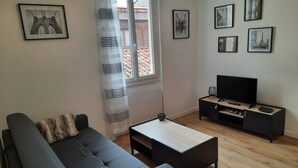A living room with a sofa, a coffee table, a TV stand, and framed pictures on the wall. - The black and white nice studio hyper center and wifi (Toulouse)