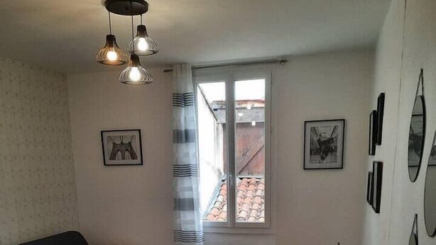 A compact living space with a sofa, a small table, and a dining area. There are framed pictures on the walls and a window with a view of a building outside. - The black and white nice studio hyper center and wifi (Toulouse)