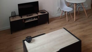 A modern living room with a flat-screen TV, a coffee table, and a dining area with a white table and chairs. - The black and white nice studio hyper center and wifi (Toulouse)