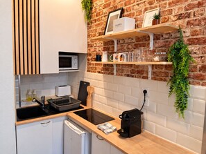A kitchen with a brick wall, white cabinets, a microwave, a toaster, a coffee maker, and a hanging plant.