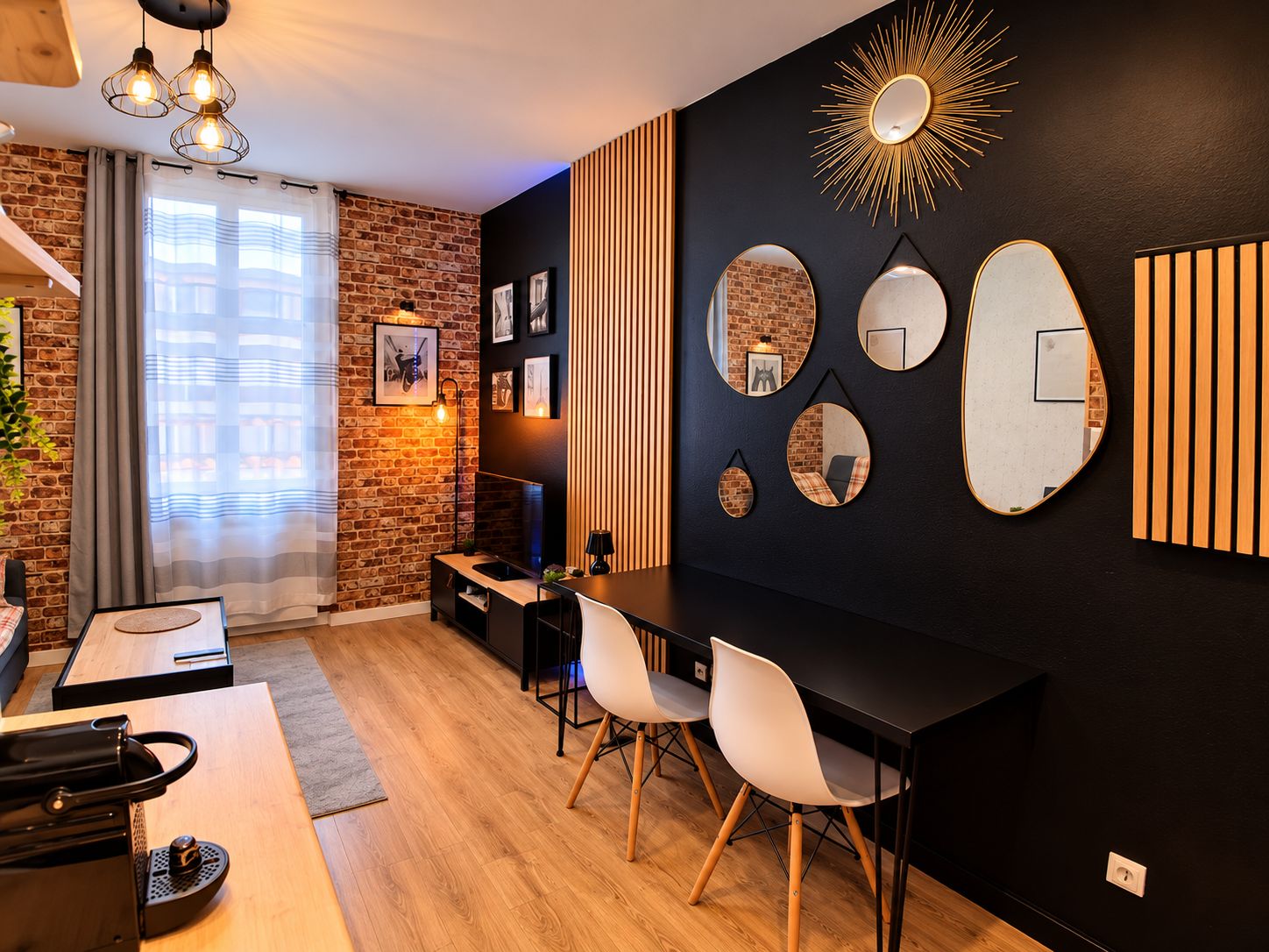 Una sala moderna con pared de ladrillo, pared negra con espejos y una mesa de comedor de madera con sillas.