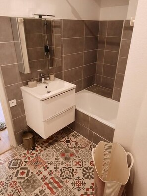 A bathroom with a white sink, a mirror, a shower, and a patterned floor.
