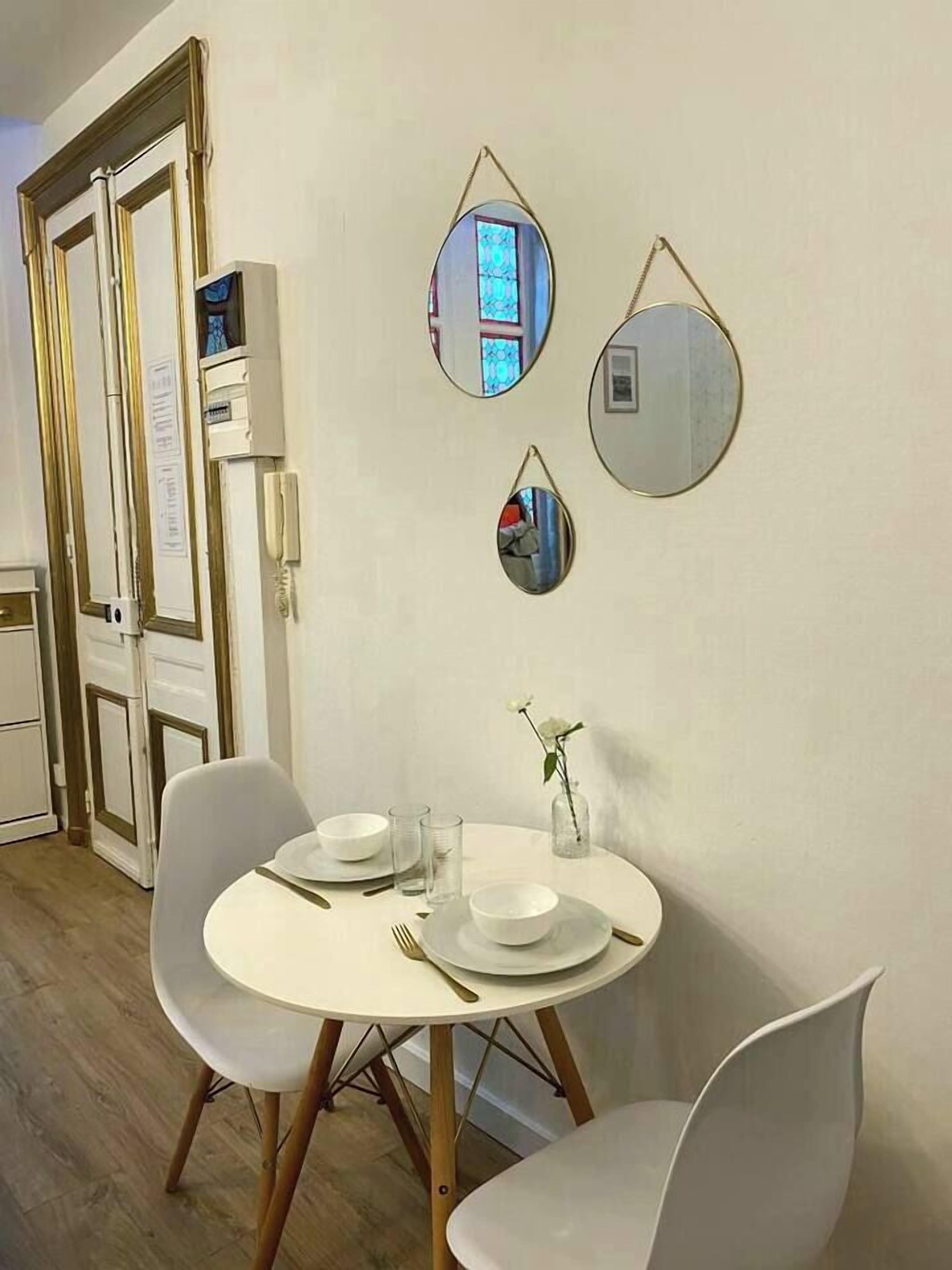 Un coin repas avec une table ronde, des chaises blanches et un vase contenant une seule fleur.