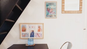 Una habitación con una mesa de madera oscura, dos sillas color beige, un cuadro enmarco con varias ilustraciones y un pequeño jarrón azul.