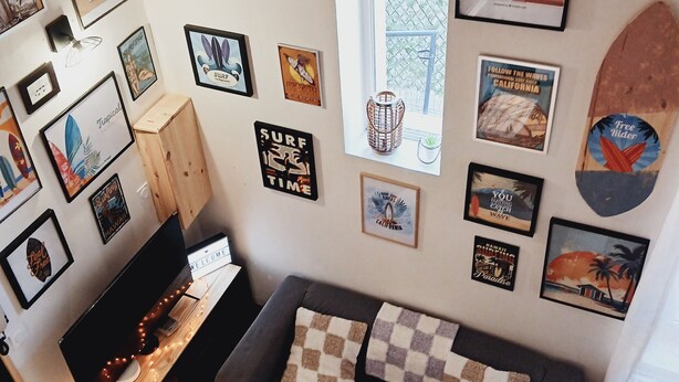 Una sala de estar con un sofá gris, una mesa de centro de madera y varios carteles enmarcados con temática de surf en las paredes.