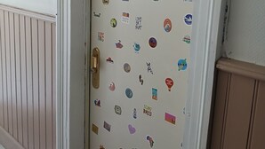Una puerta decorada con varios adhesivos de temática viajera, incluyendo destinos turísticos e imágenes relacionadas con el surf.