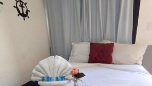 A hotel room with a bed, a white wall with a ship's wheel decoration, a black bedspread, a white towel, a glass jar with a rose, and a red pillow. - Pousada Maresia Praia (Rio das Ostras)