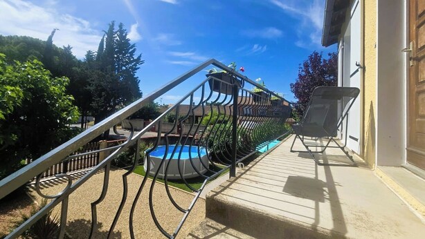A pool area with a staircase leading to a deck, surrounded by greenery.