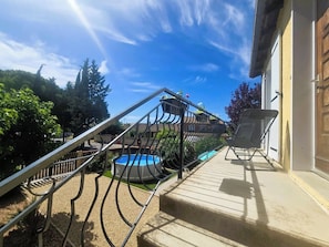 A pool area with a staircase leading to a deck, surrounded by greenery.