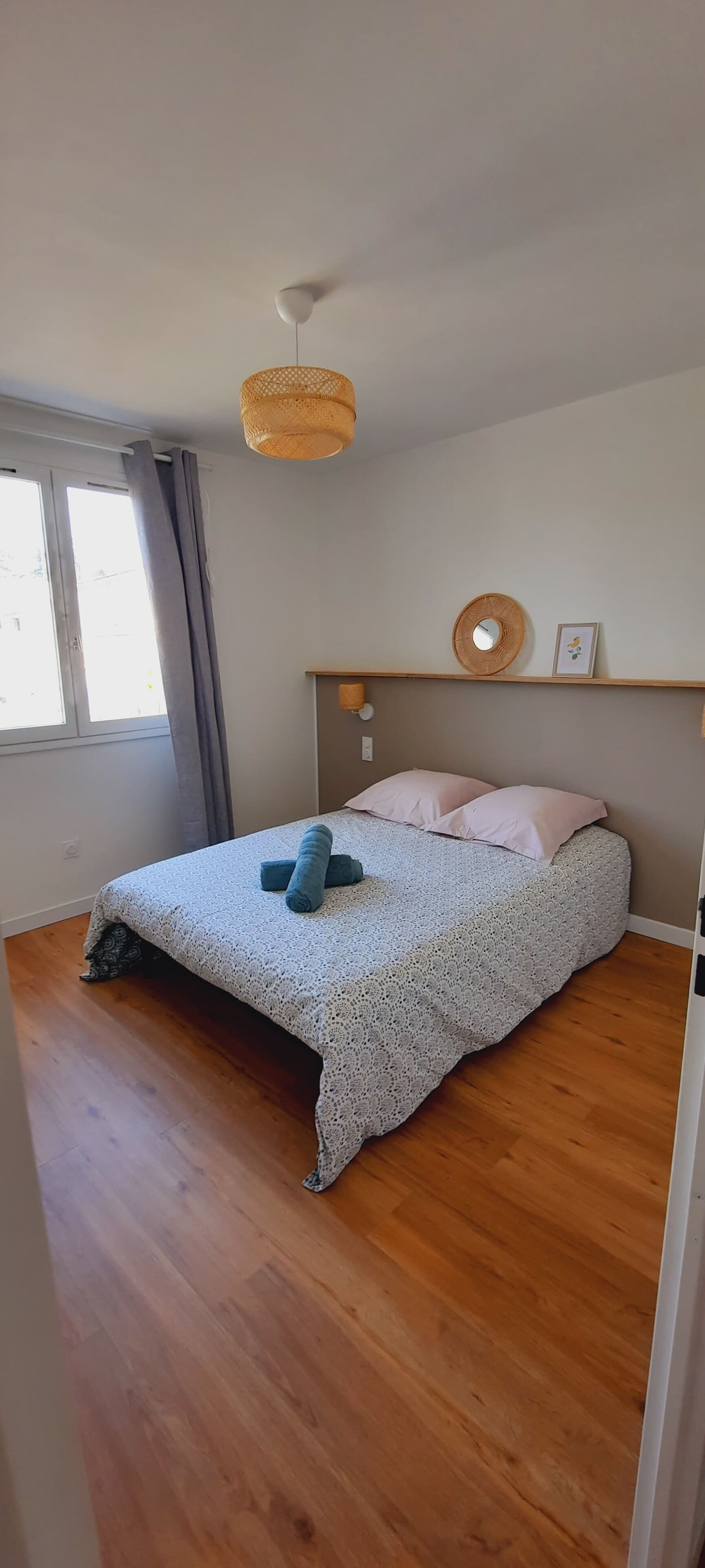 A bedroom with a large bed, a ceiling fan, a window with curtains, and a wooden floor.