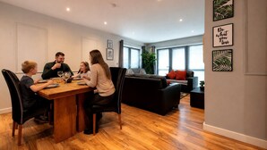 A modern dining area with a wooden table, black chairs, and a black sofa in the background. - 2 Bedroom Accessible Step-Free Central  (Liverpool)