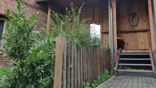 A wooden porch with a brick wall and a wooden door. - Living in a small village in the middle of nature many lakes forest and hiking trails (Friedland)