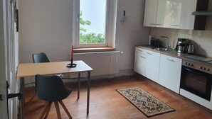 A compact kitchen with white cabinets, a built-in oven, and a window with a view of greenery. - Living in a small village in the middle of nature many lakes forest and hiking trails (Friedland)