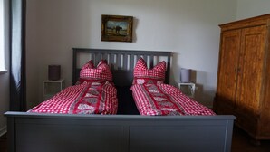 A bedroom with a double bed, two bedside tables, a wooden wardrobe, and a framed picture on the wall. - Living in a small village in the middle of nature many lakes forest and hiking trails (Friedland)