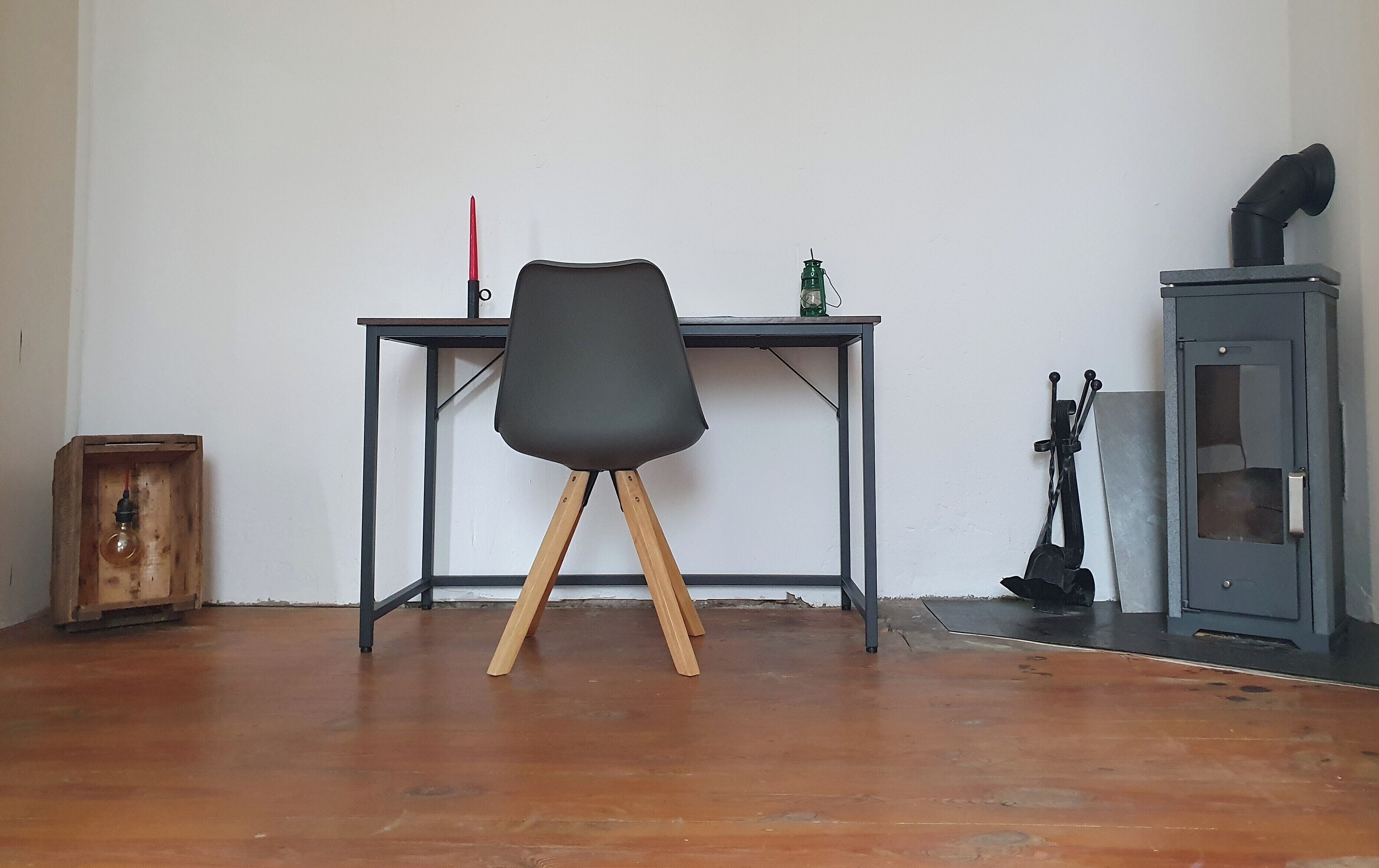 Una stanza con pavimento in legno, una scrivania con sedia, un armadio e una piccola scatola di legno.