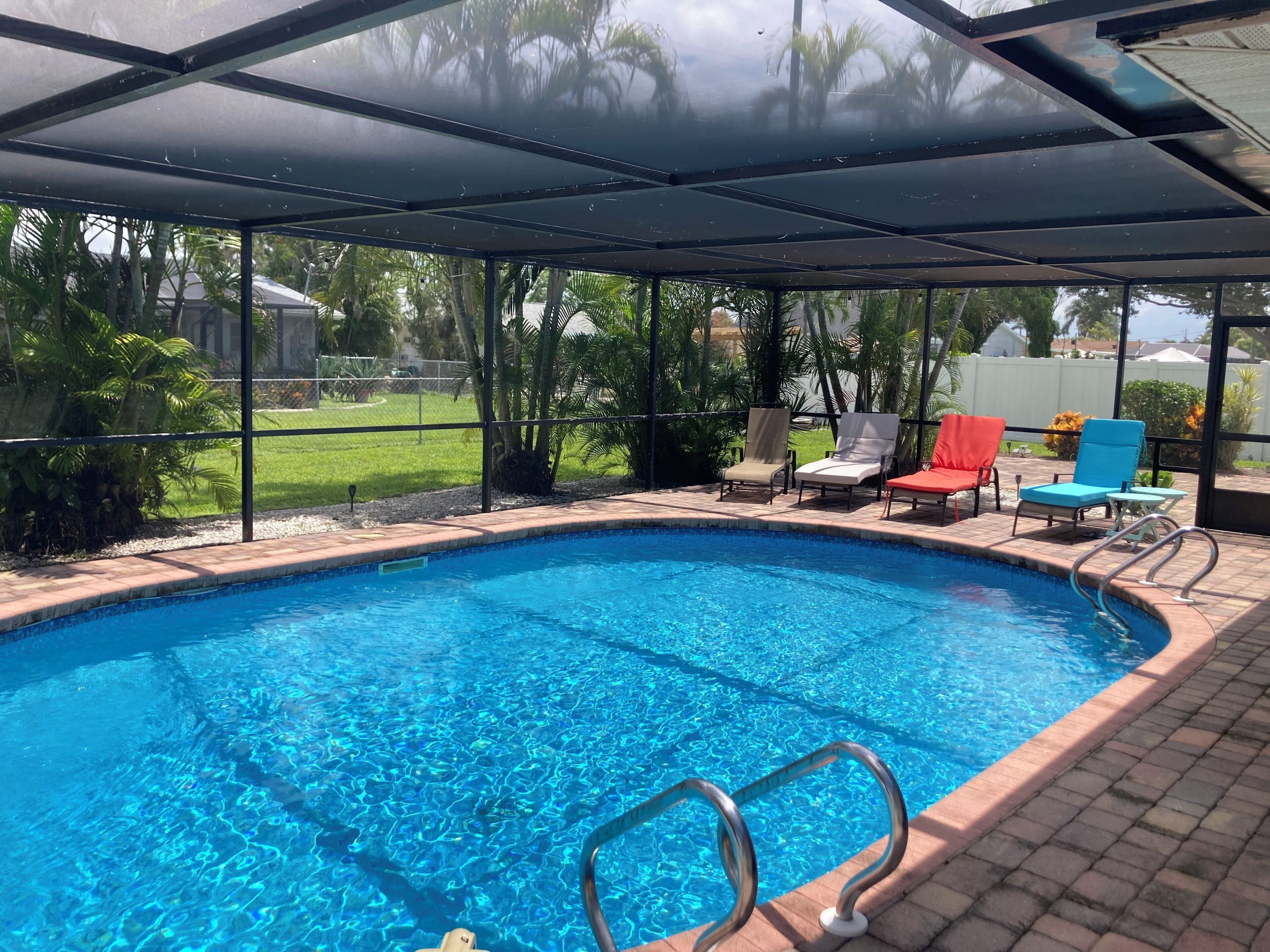 A covered swimming pool with clear blue water, surrounded by lounge chairs and a brick deck.