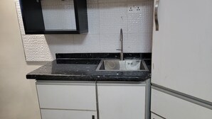 A kitchen with white cabinets, a black countertop, and a stainless steel sink. - Standard Room #14 (Ikeja)