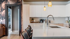 A modern kitchen with white cabinets, a central island, pendant lighting, and a dining area with leather chairs.