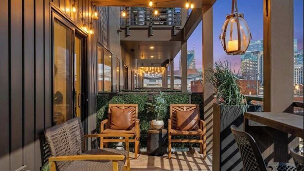 An outdoor seating area with chairs and tables, a hanging light fixture, and a view of the cityscape.