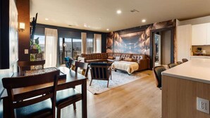 A modern living room with a sofa, a dining table with chairs, a kitchen area, and a large window with curtains.