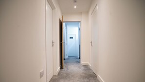 Un couloir étroit, doté d’un revêtement de sol en moquette et de murs blancs, qui mène à une porte au fond.