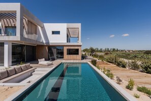 Ett modernt hus med en swimmingpool, ett trädäck och en utomhusplats med sittmöbler.