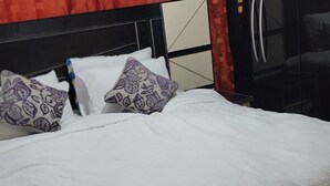 A bed with white bedding and patterned pillows, a black headboard, and a red curtain. - Super Deluxe Room #1 (Ikeja)