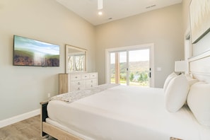 A bedroom with a bed, a dresser, a mirror, a television, and a sliding glass door leading to a scenic outdoor view. - Sunset Sky Lodge (McHenry)