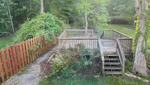 A wooden deck with a staircase leading to a raised platform, surrounded by a wooden fence and lush greenery.