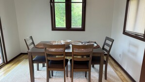 A dining area with a table set for four, surrounded by chairs, a window with blinds, and a carpeted floor.